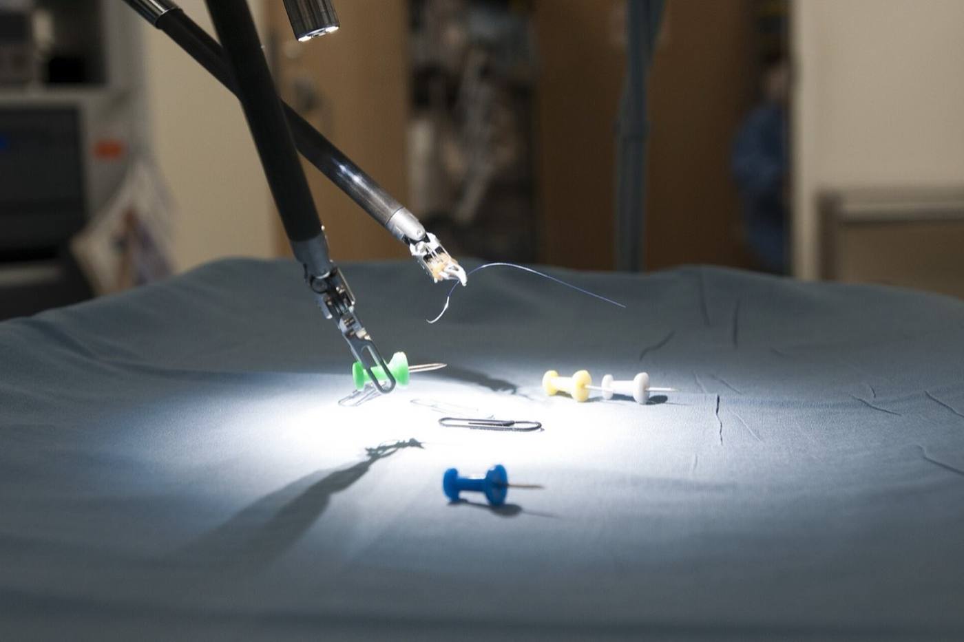 Robotic surgical instruments manipulating small objects on a surgical drape under theatre lights.